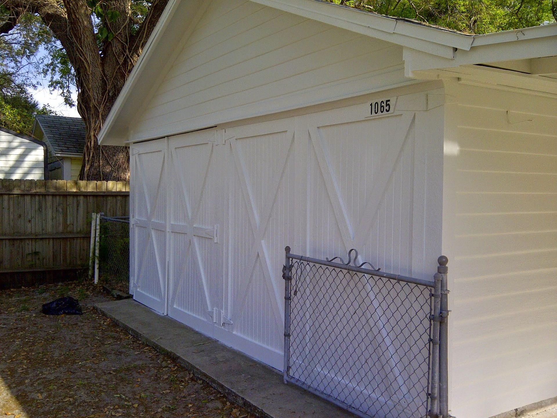 White garage with closed doors and a chain-link gate in a fenced backyard