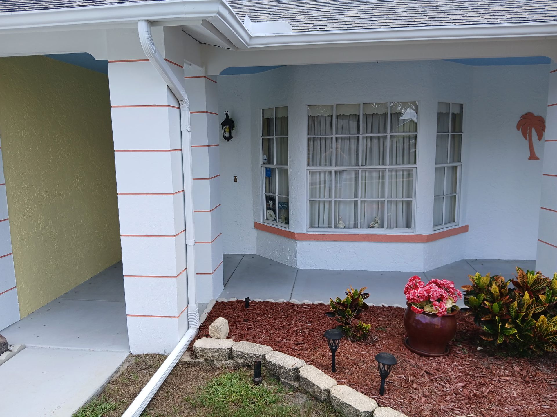 Front entrance of a house with light blue walls, white trim, and a small landscaped front garden.