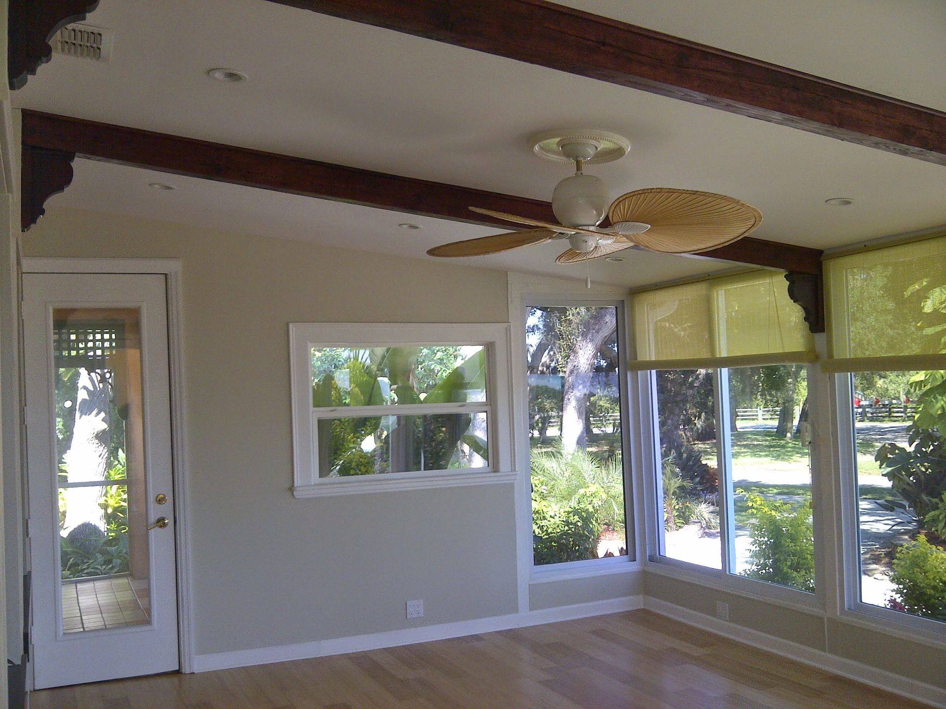 Empty sunroom with large windows, beige walls, a ceiling fan, and sunlight streaming in.