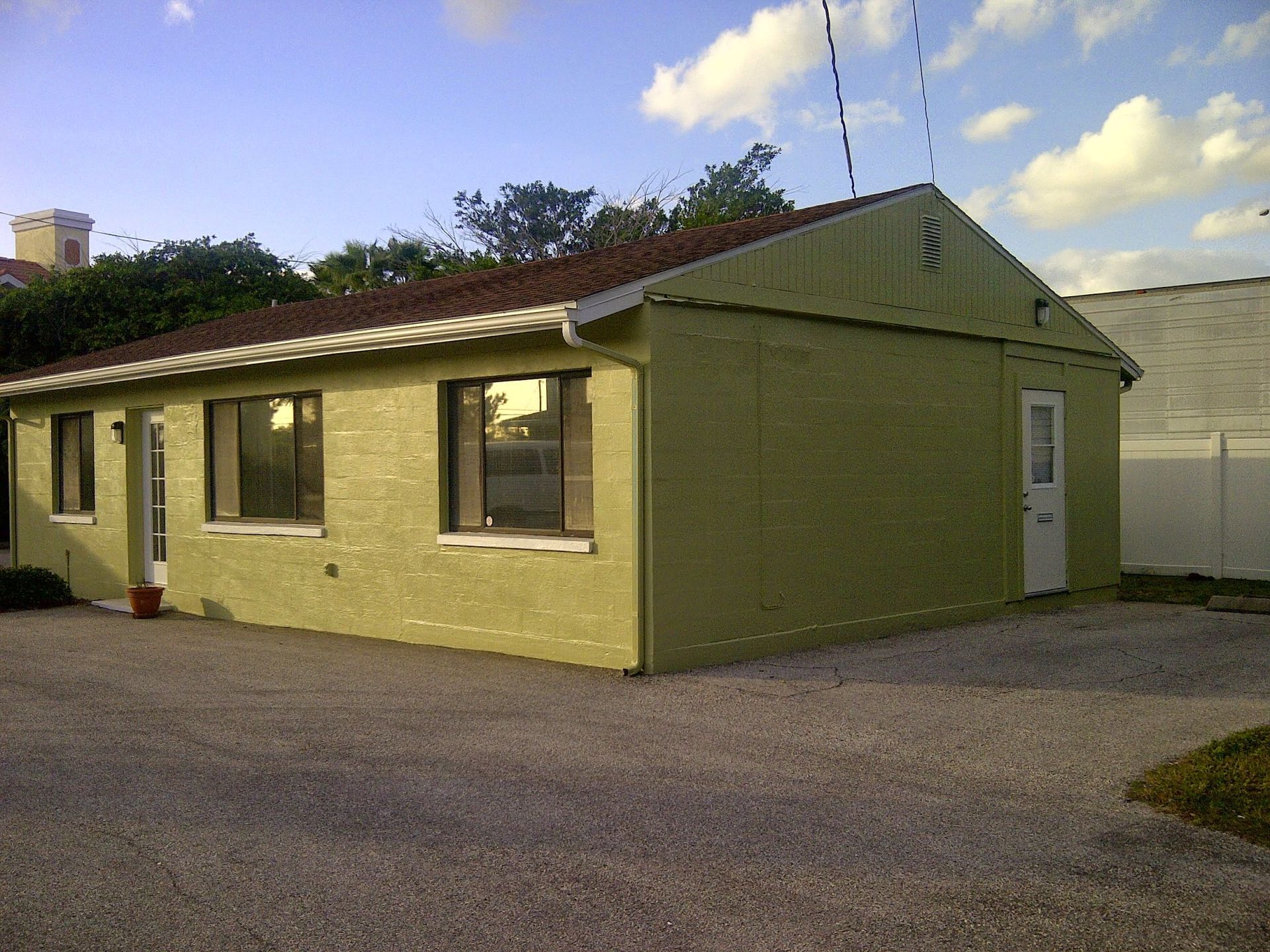 Single-story yellow building with brown roof and gravel driveway under a partly cloudy sky