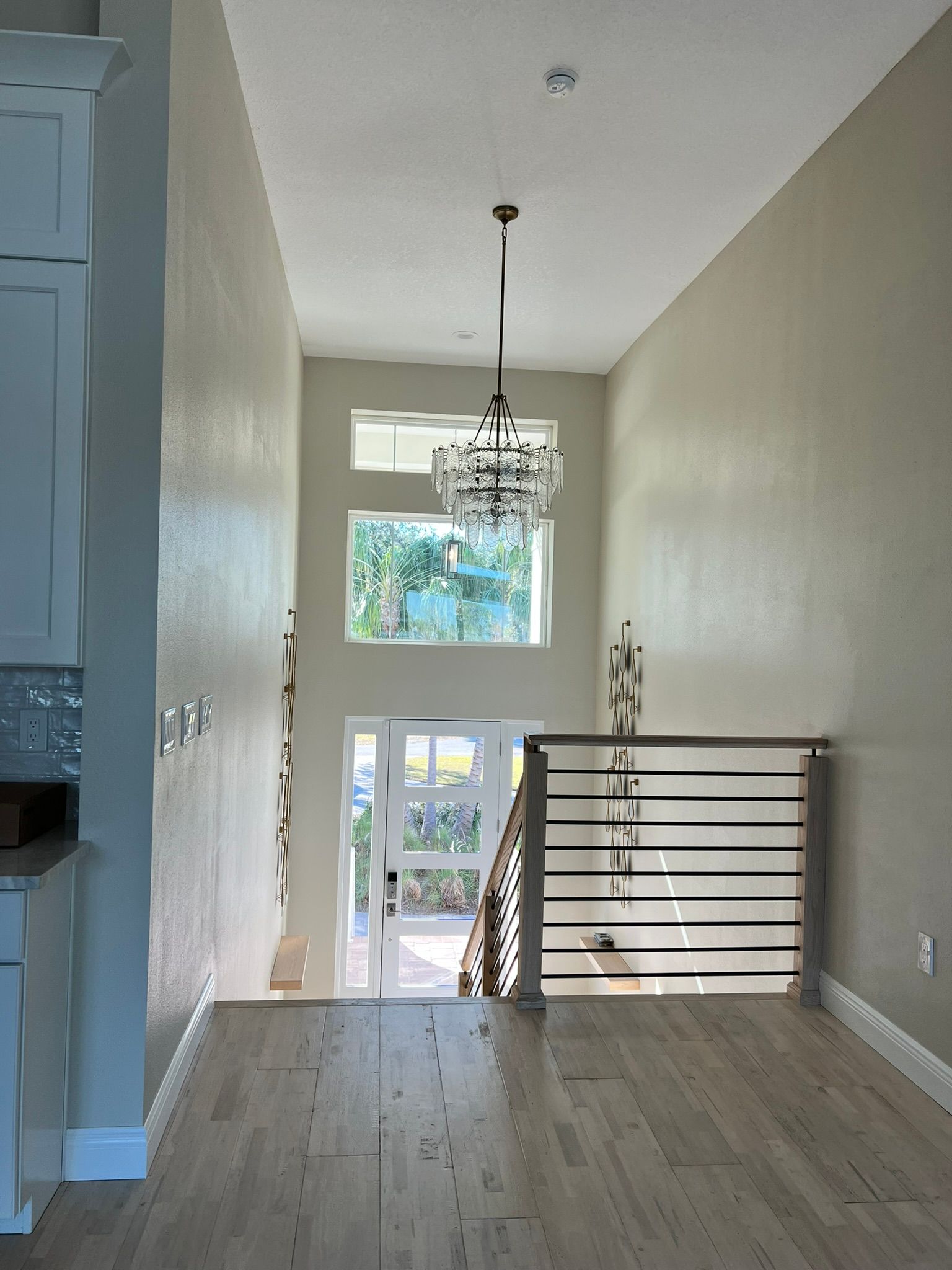 Bright hallway with hardwood floors, white walls, chandelier, and a railing overlooking a stairwell.