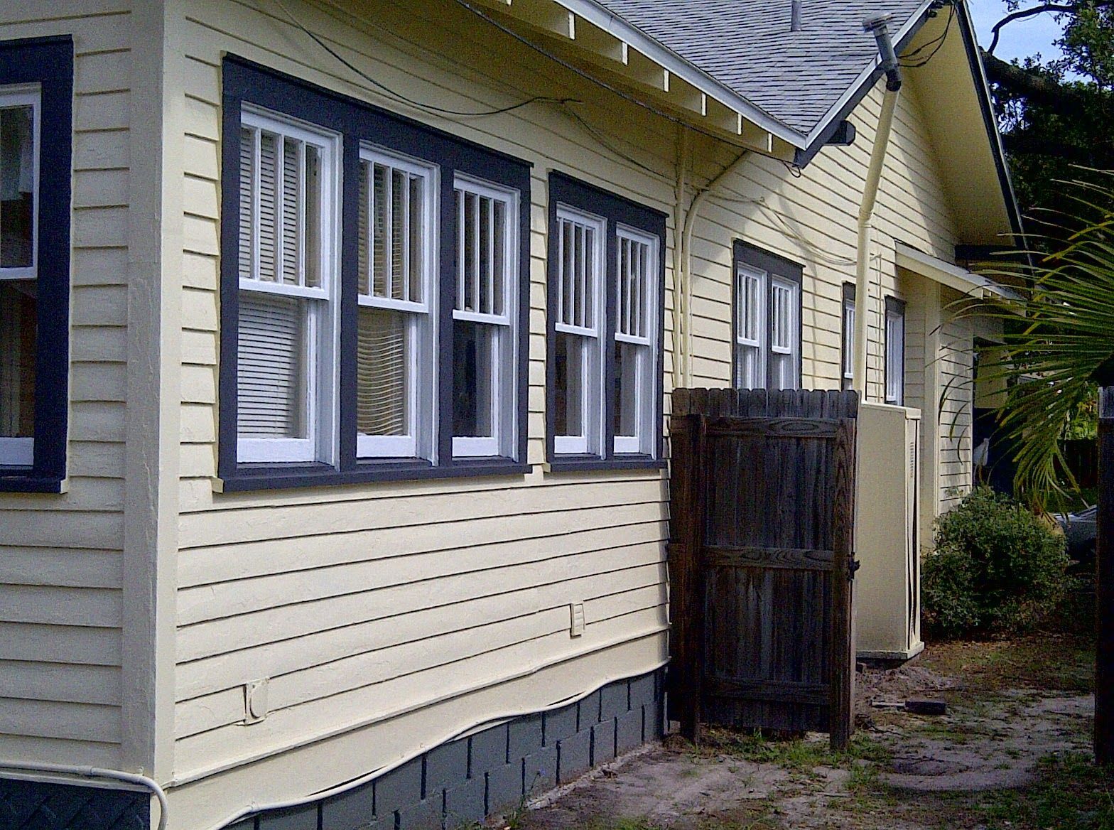 Yellow house exterior with blue-trimmed windows, siding, and a small fenced entryway