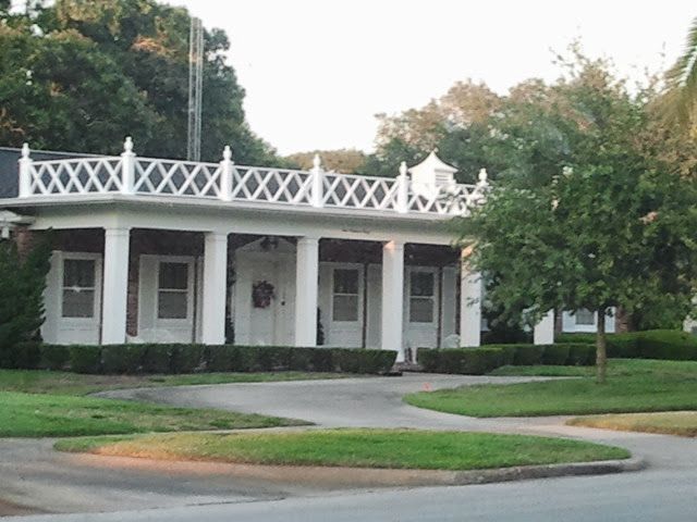 White pavilion-style building with columns and decorative railing, surrounded by grass and trees.