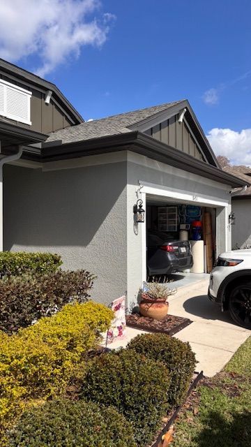 Suburban house exterior with open garage, driveway, and trimmed shrubs under a blue sky