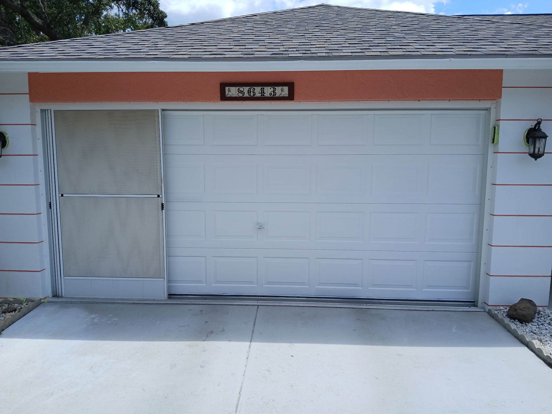 Closed white garage door with a small address plaque above it and a white side entrance curtain.