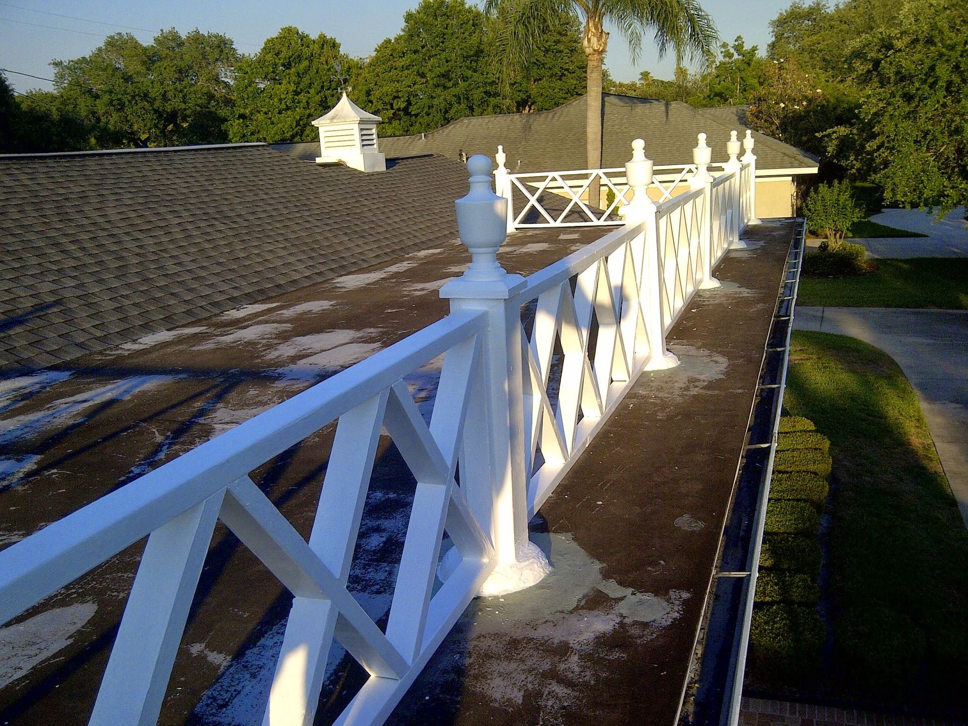 White wooden fence along a rooftop walkway beside trees in warm sunlight