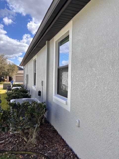 Exterior of a light gray house with white-trimmed windows, bushes, and a mulch bed along the wall
