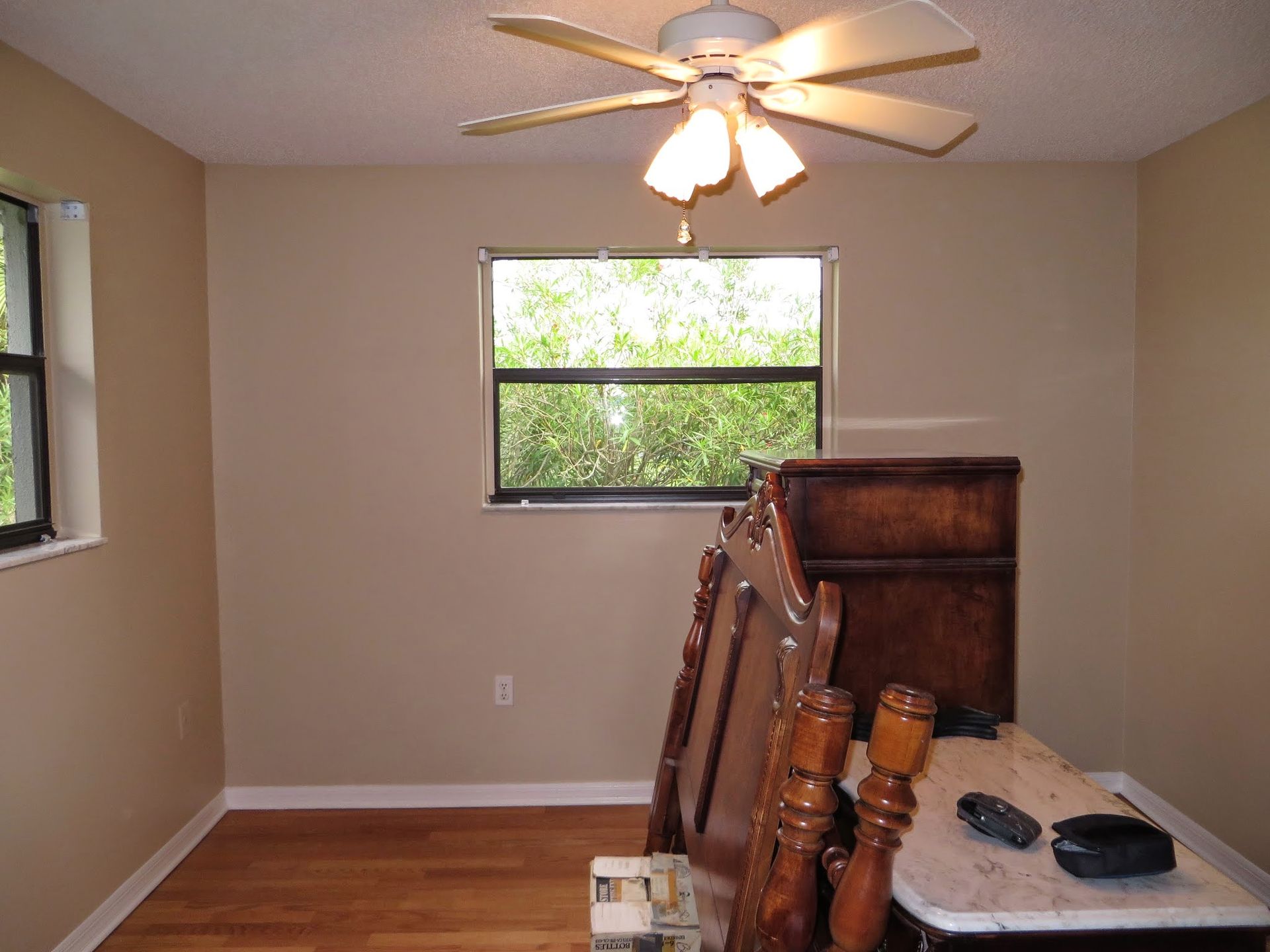 Empty beige room with ceiling fan, two windows, and a stack of furniture in the foreground
