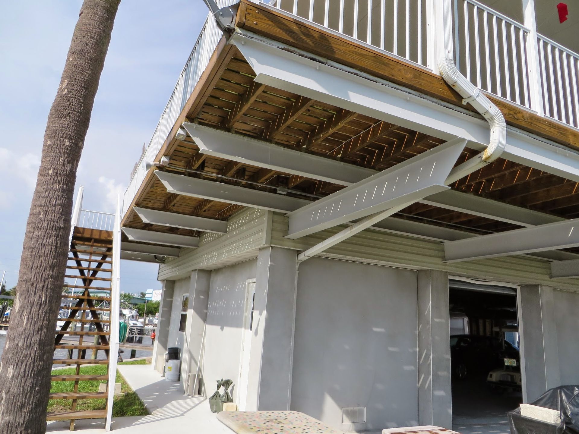 Under-deck view of a raised house with white siding and stairs beside a palm tree