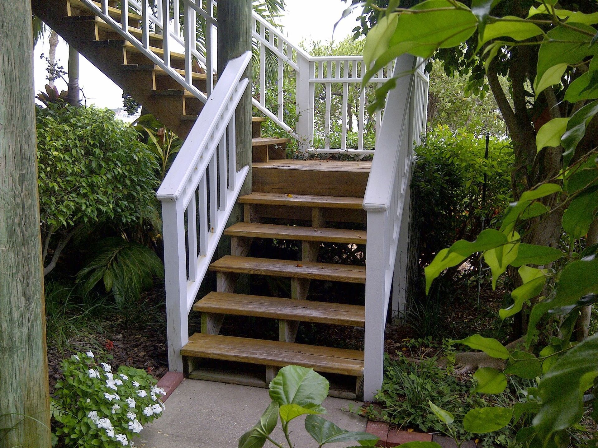 Wooden outdoor staircase with white railings leading up a garden path