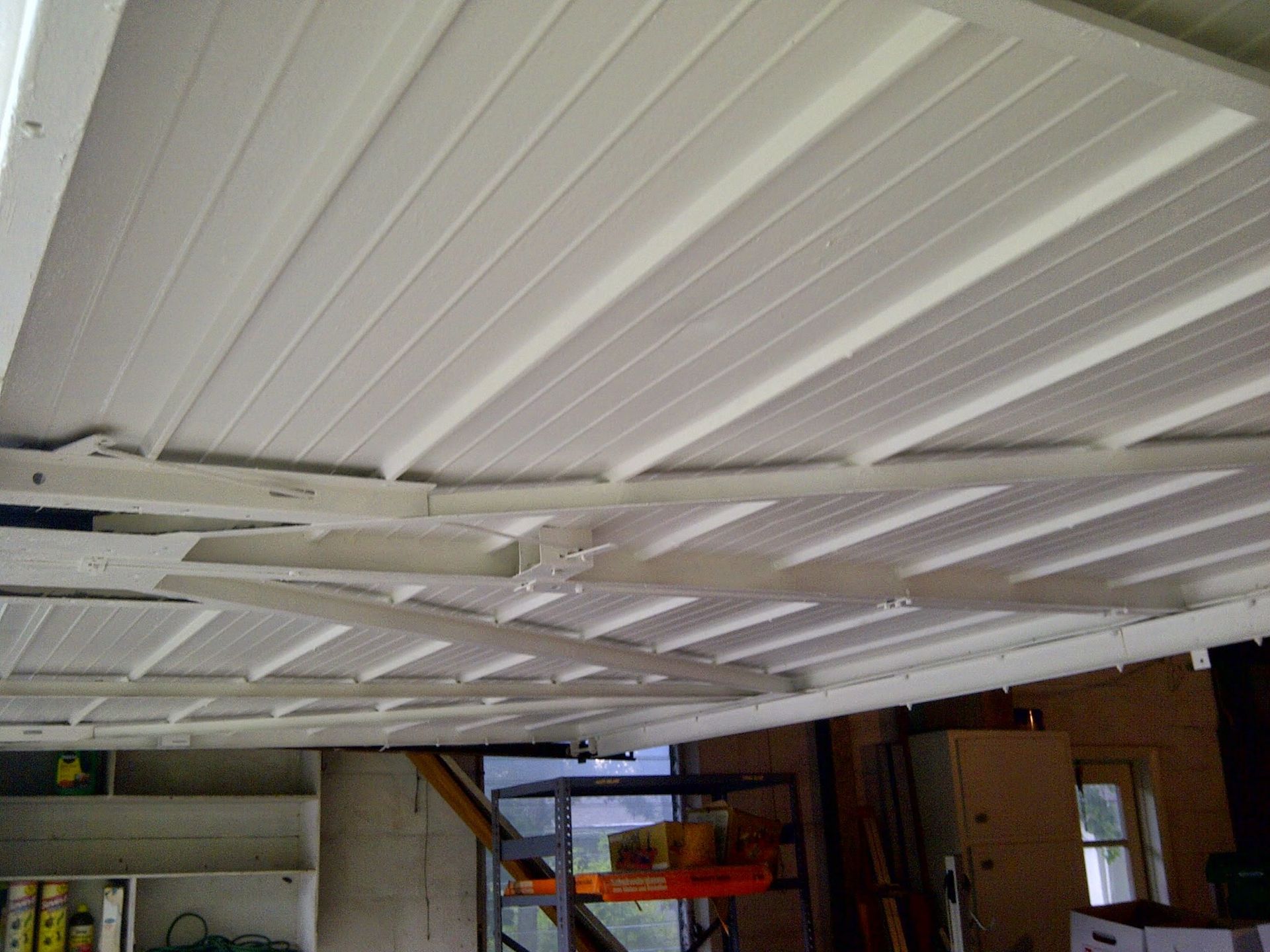 White paneled garage ceiling with exposed beams and a shelf in the back corner