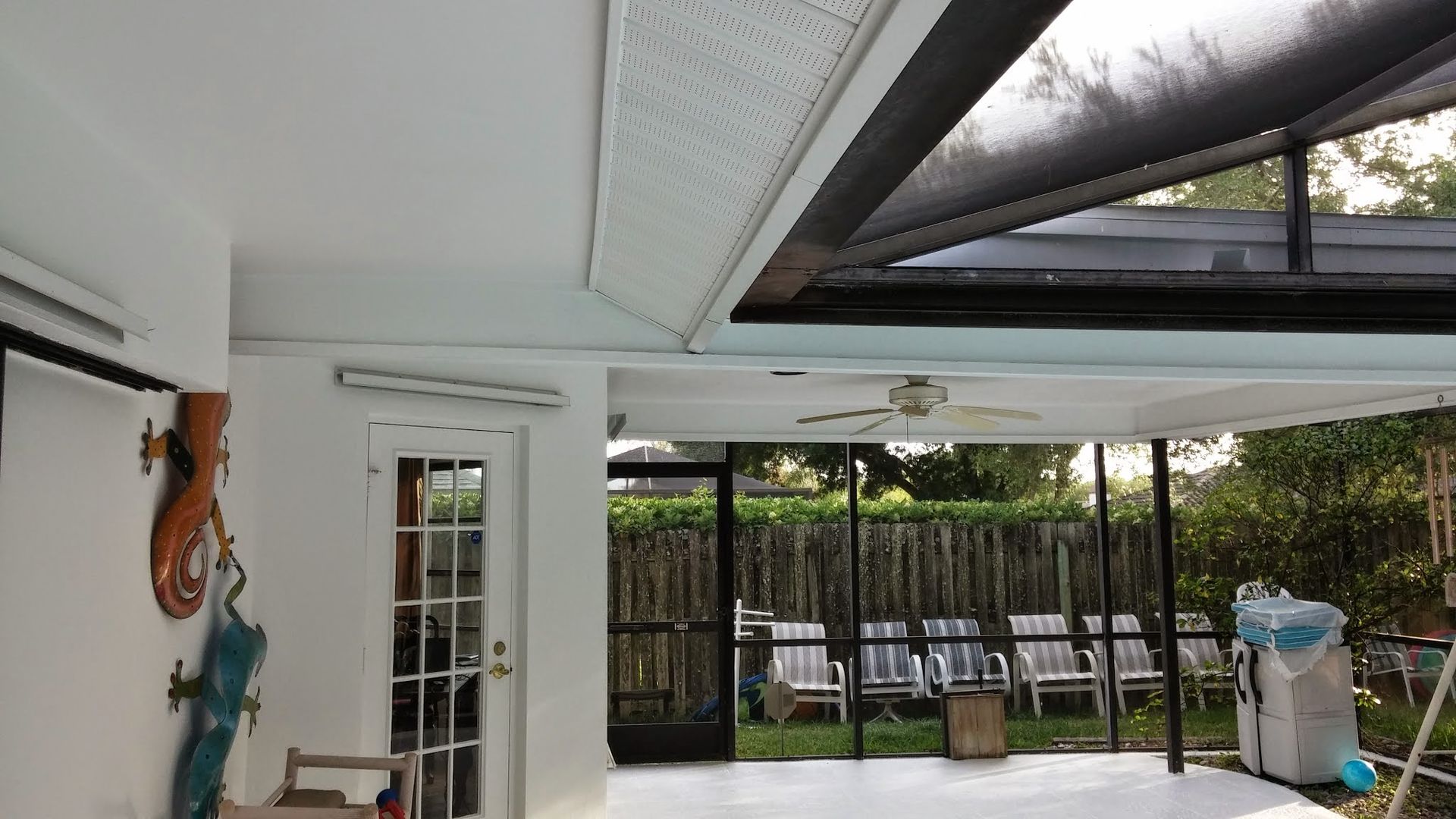 Covered patio with white chairs, glass door, and a partially open roof overlooking a yard.