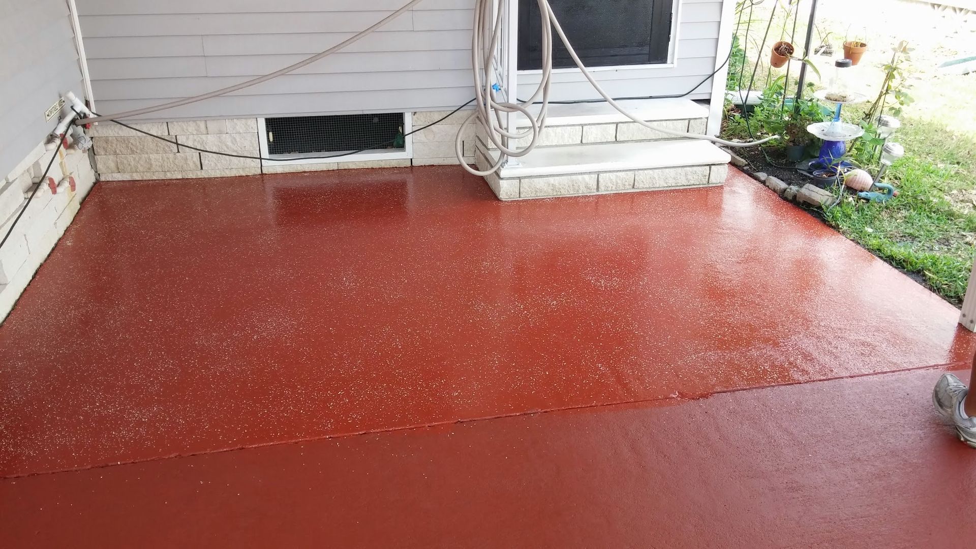 Red painted patio beside a house with strings of lights and a small garden bed on the right.