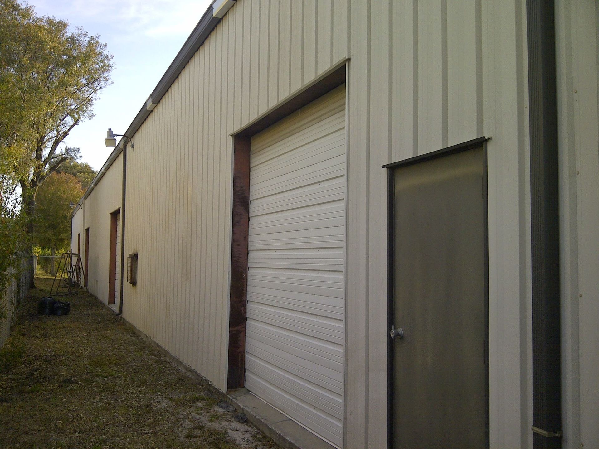 Side view of a beige metal warehouse with a roll-up door and a small side entrance