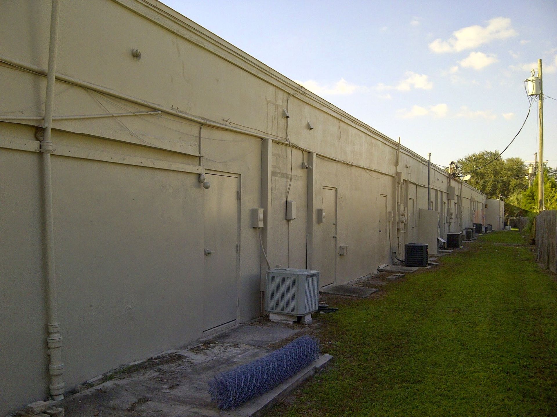Long beige industrial building beside a grassy strip under a partly cloudy sky