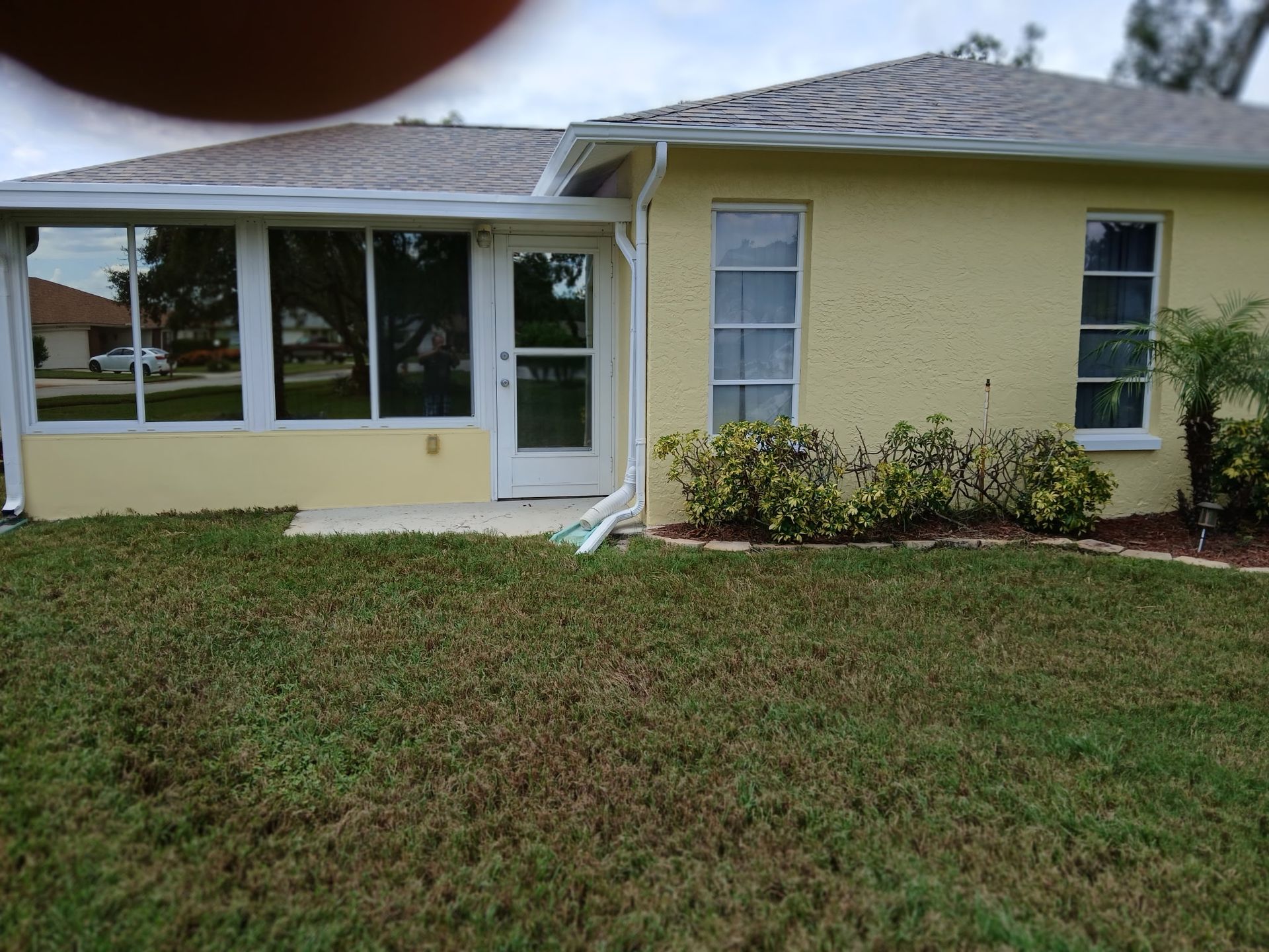 Single-story yellow house with screened porch, white door, and grassy front yard