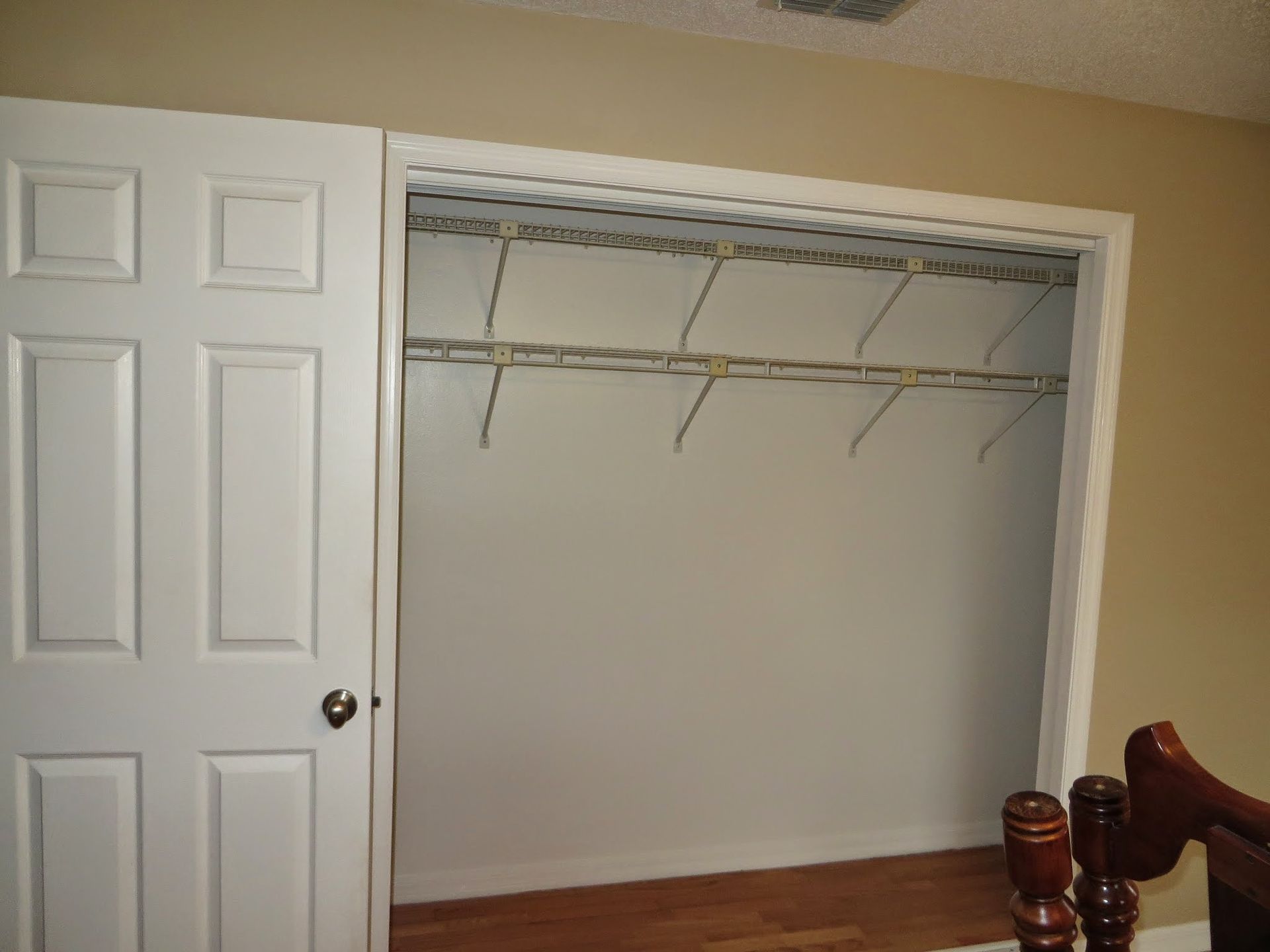 Open closet with white sliding doors and wire shelving in a beige bedroom.