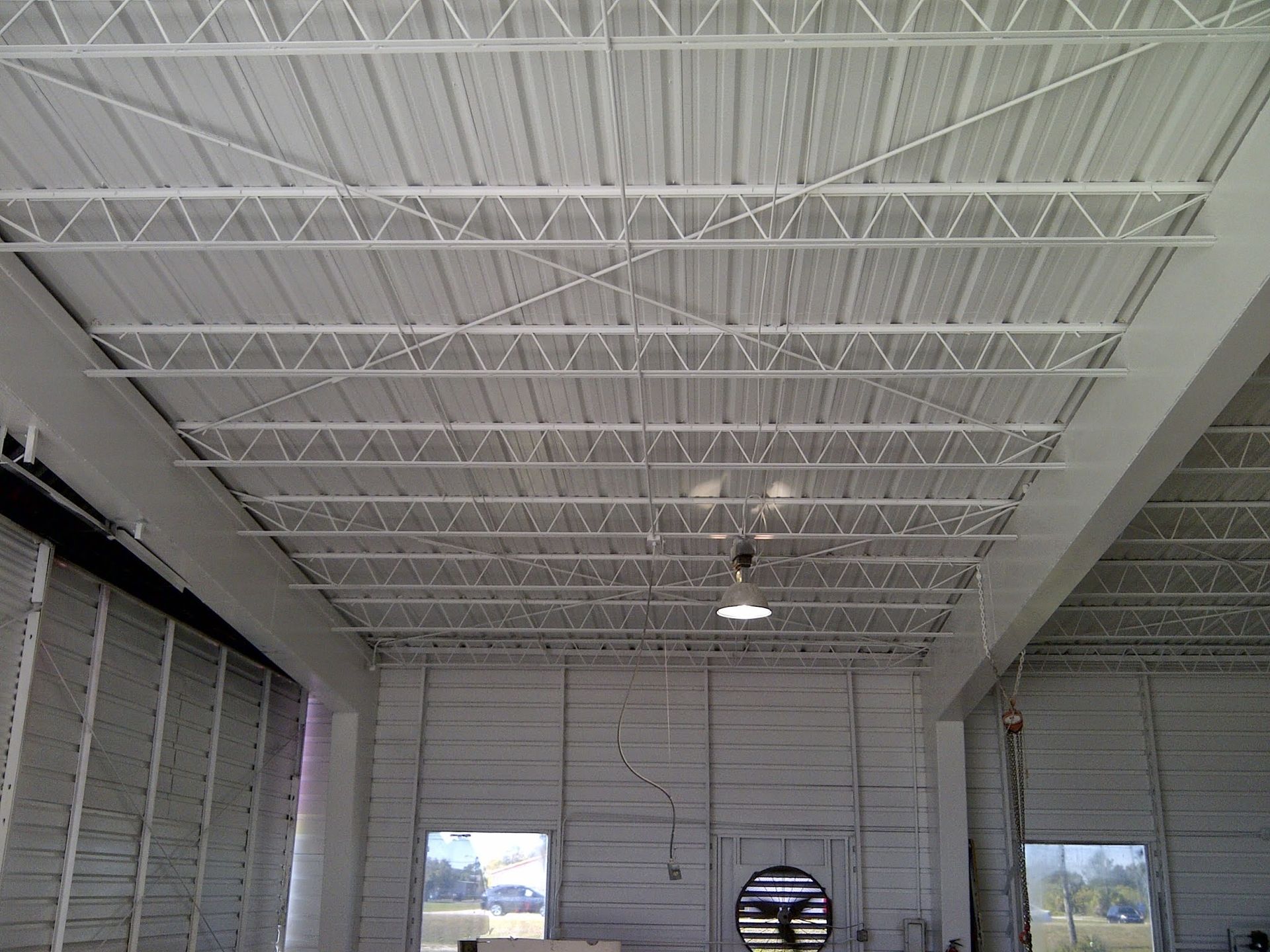 Empty industrial warehouse with white ceiling trusses and skylights, viewed from inside