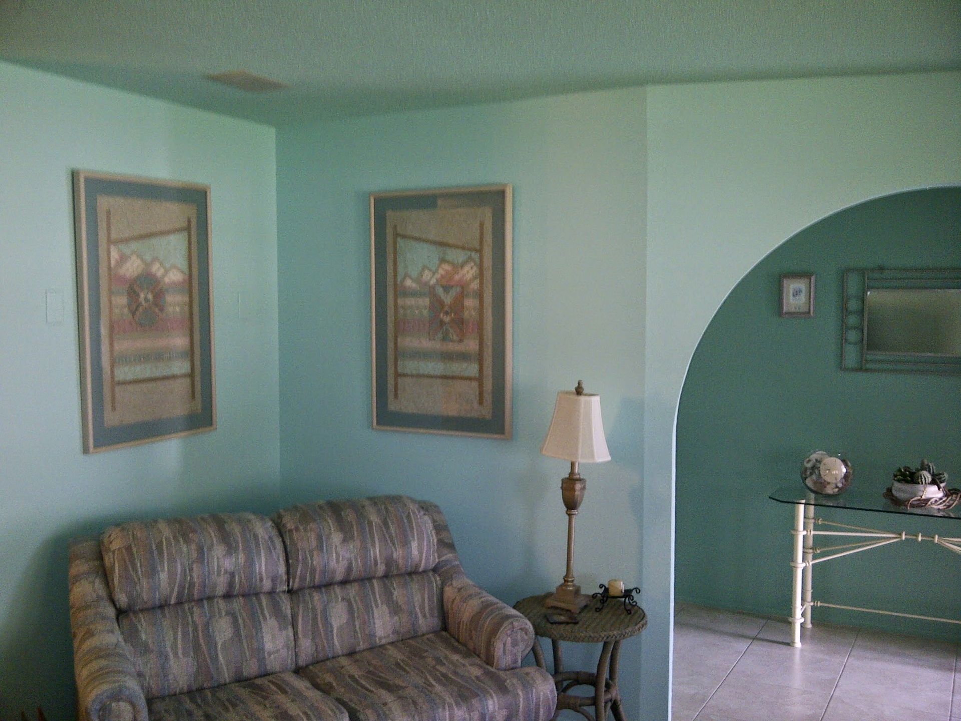Living room with plaid sofa, lamp, framed art, and a green arched alcove with a small table