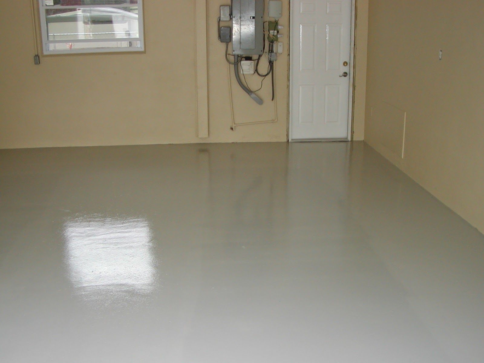 Empty beige room with glossy white floor, window, electrical panel, and closed white door