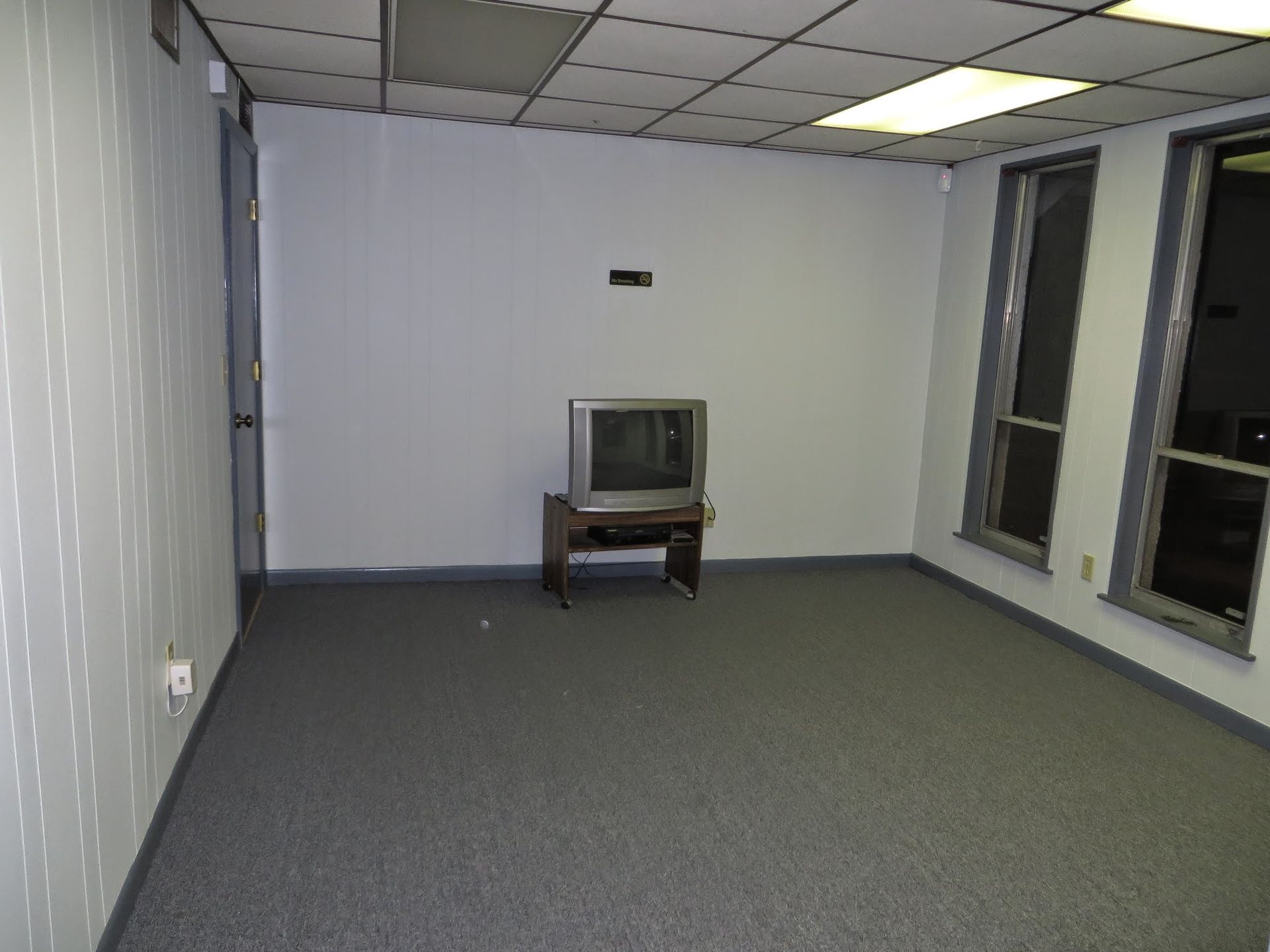 Empty room with gray carpet, white walls, windows, and a small TV on a stand.