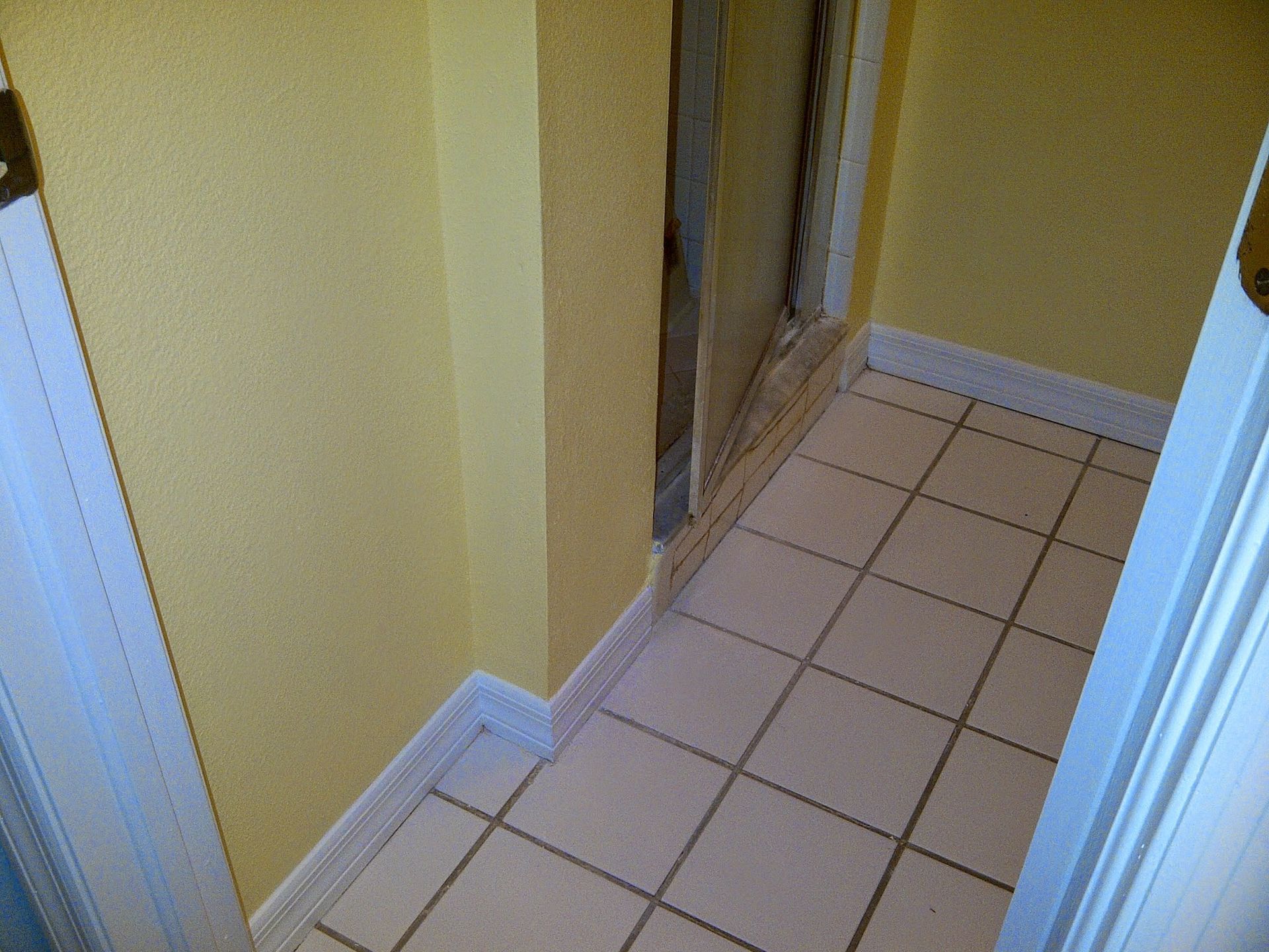 Narrow tiled hallway with yellow walls and a doorway at the end