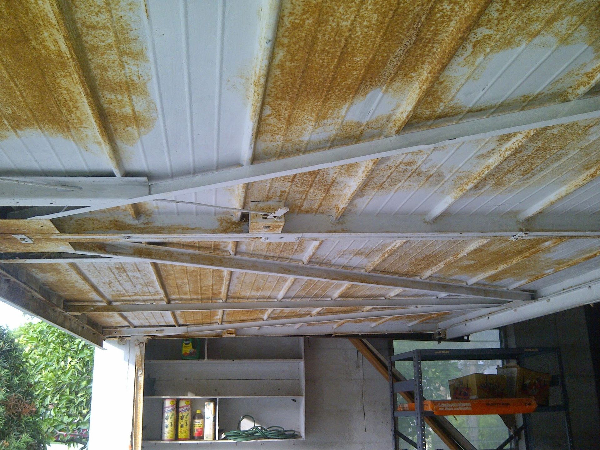 Under-house storage area with peeling ceiling paint, shelves, and a parked vehicle on the right.