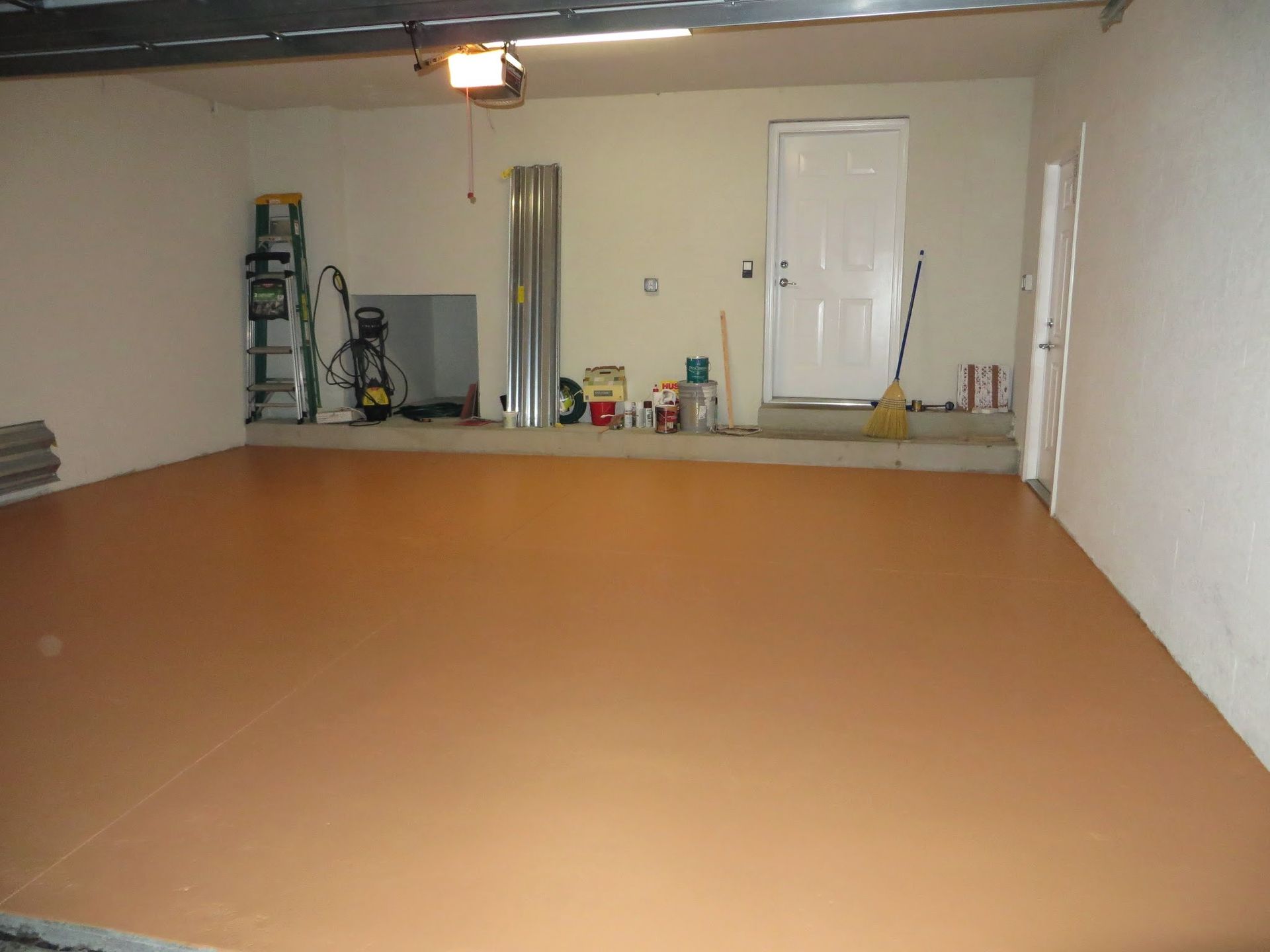 Empty garage with a smooth tan floor, white walls, and a closed door at the back.