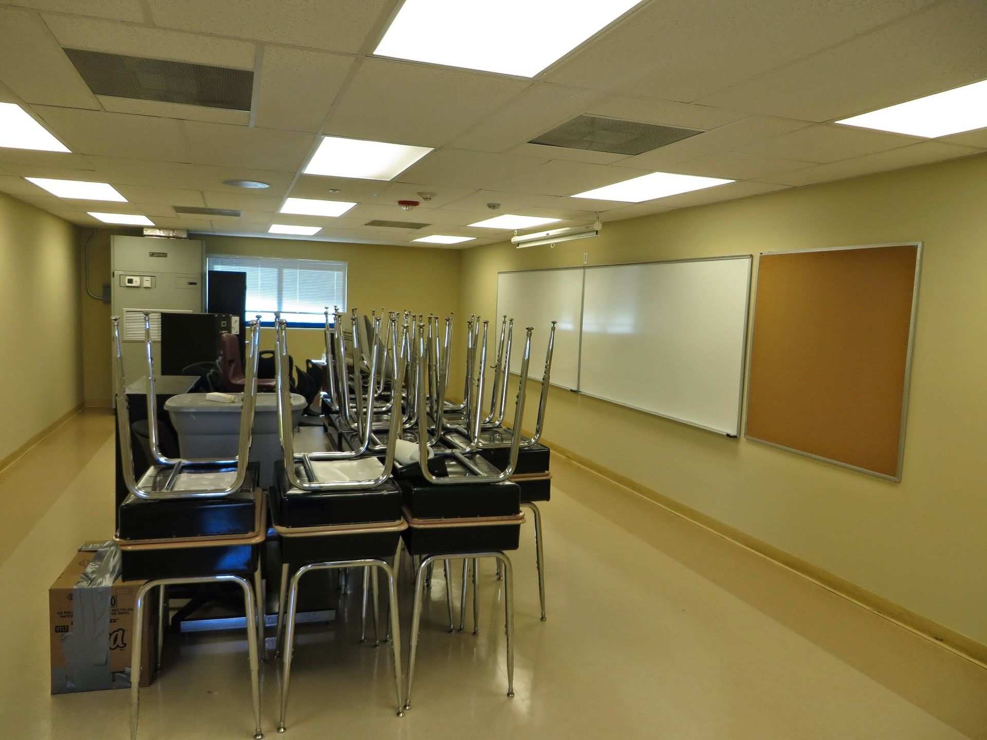 Empty classroom with stacked chairs on desks and a whiteboard along the wall