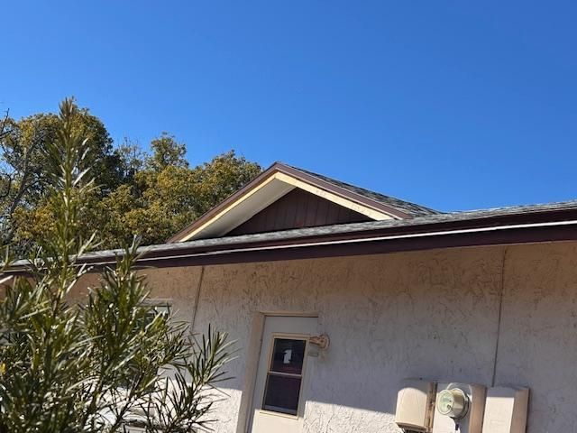 Single-story stucco house with beige trim, white door, and trees under a clear blue sky