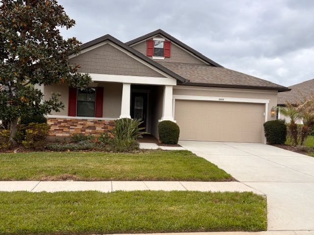 Single-story suburban house with beige siding, a two-car garage, and a front porch under a cloudy sky