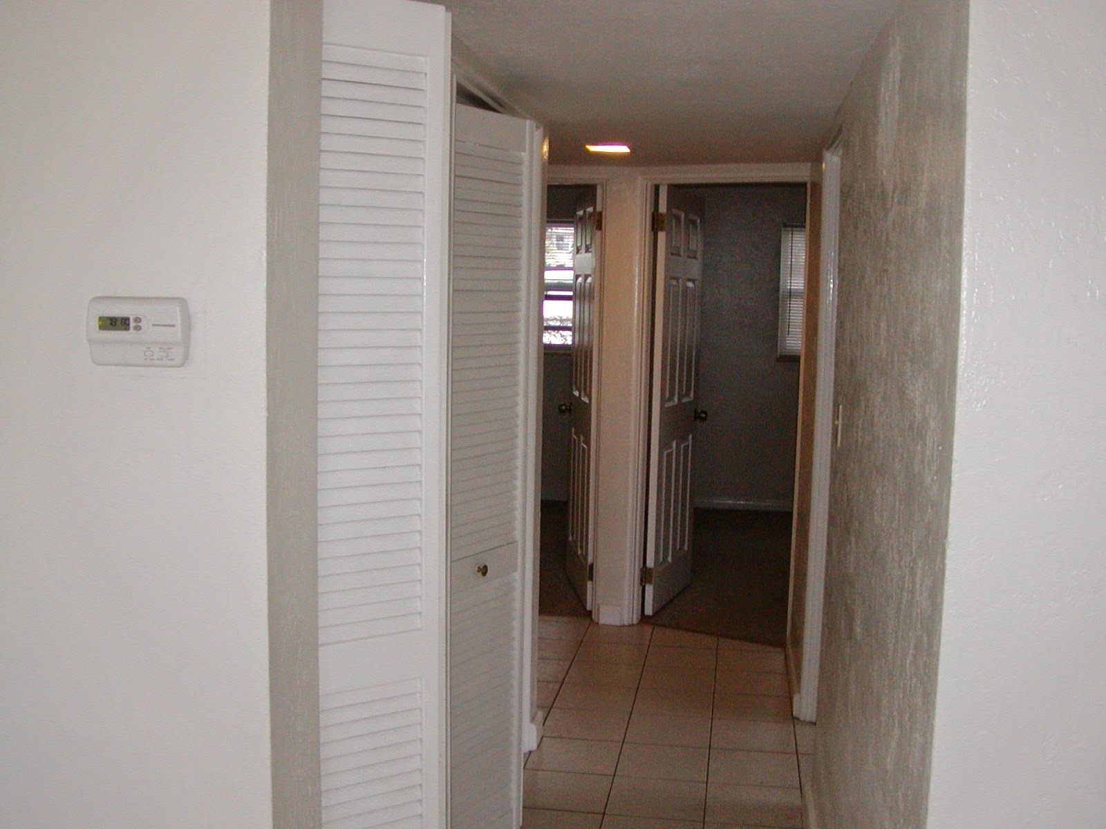 Narrow hallway with white walls, tiled floor, and a partially open louvered closet door.