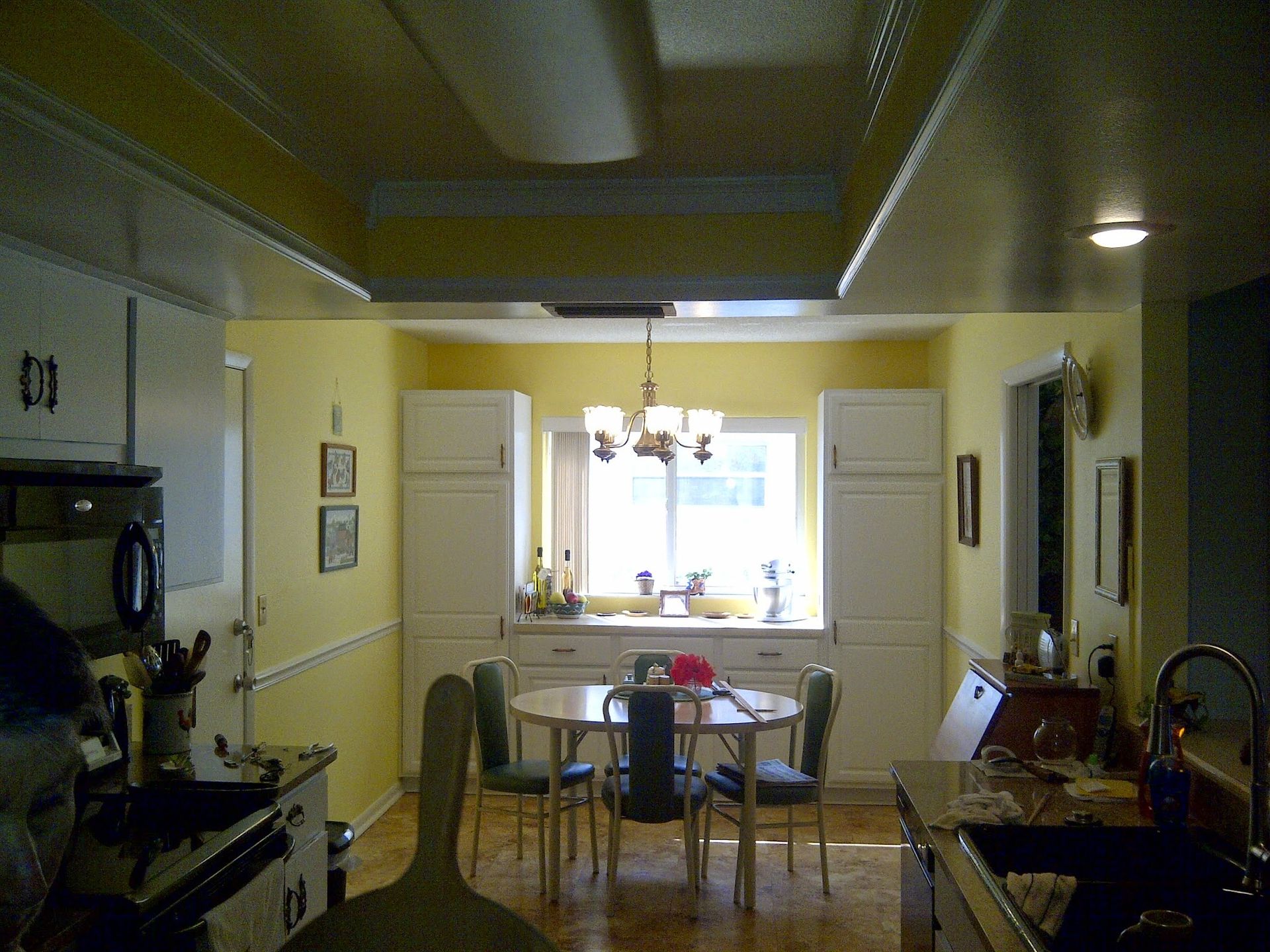 Small kitchen and dining area with white cabinets, a table, chairs, and a bright window at the far end.