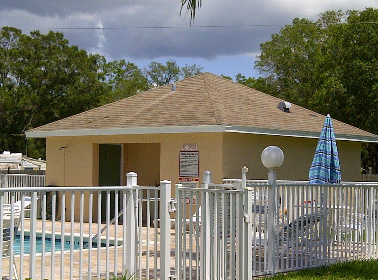 Outdoor pool house with beige walls, tiled roof, and fenced patio with tables and blue umbrella