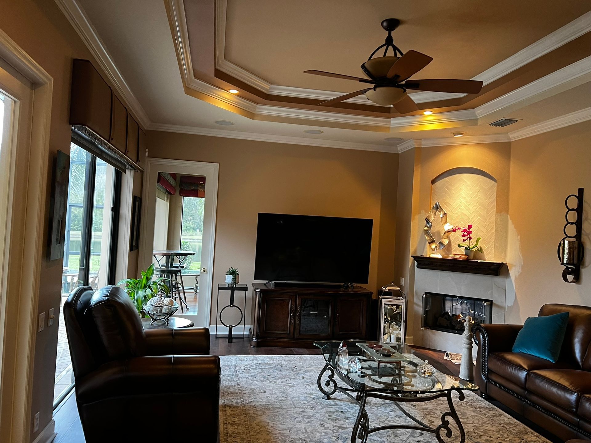 Elegant living room with leather sofas, TV, fireplace, and tray ceiling with ceiling fan