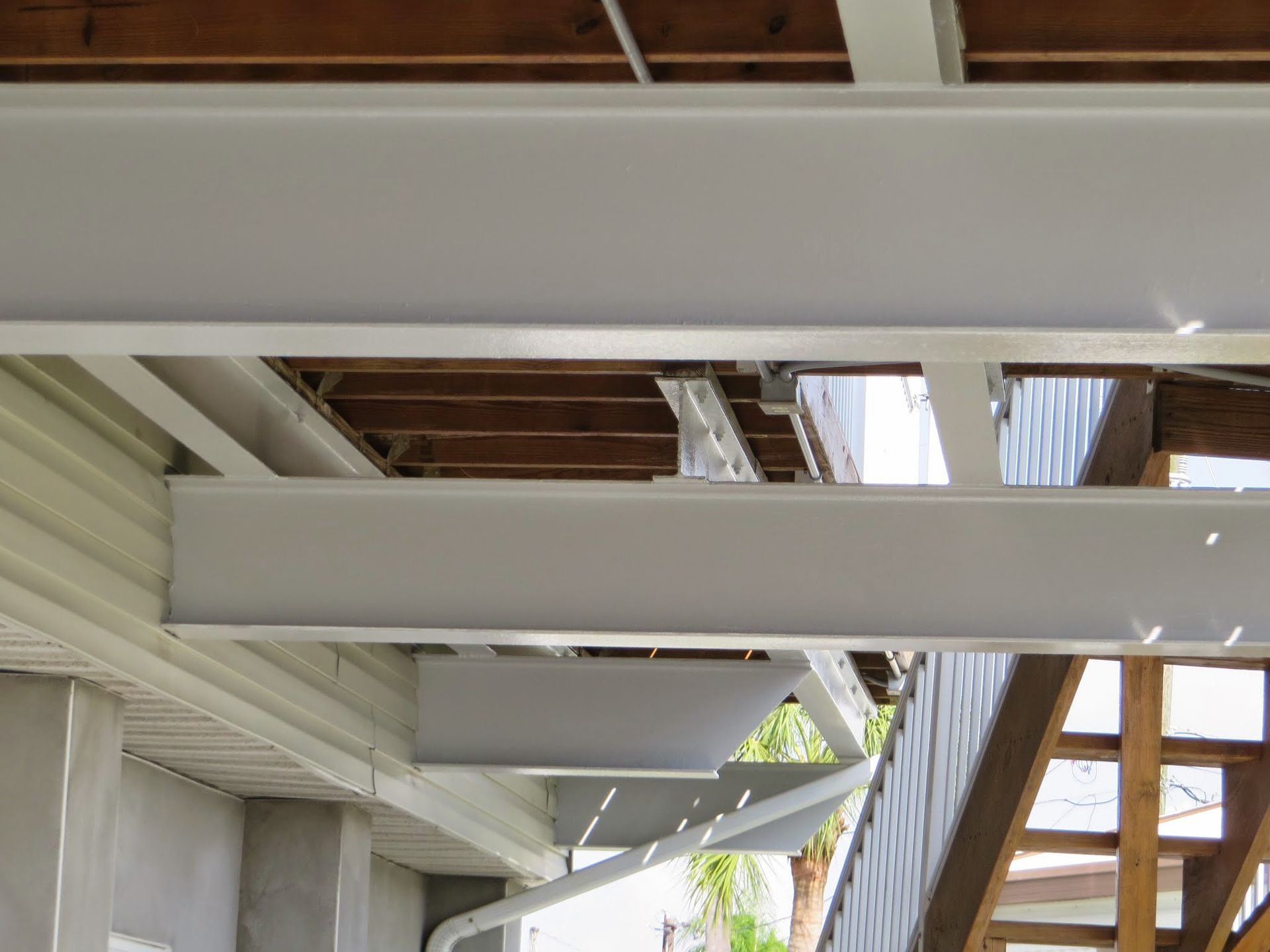 White-painted wooden beams under a porch roof with exposed rafters and a partial view of stairs and siding