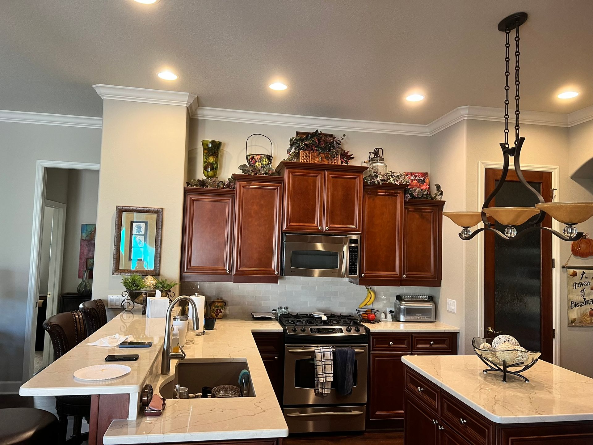 Kitchen with dark wood cabinets, stainless steel appliances, white island counter, and hanging light fixture