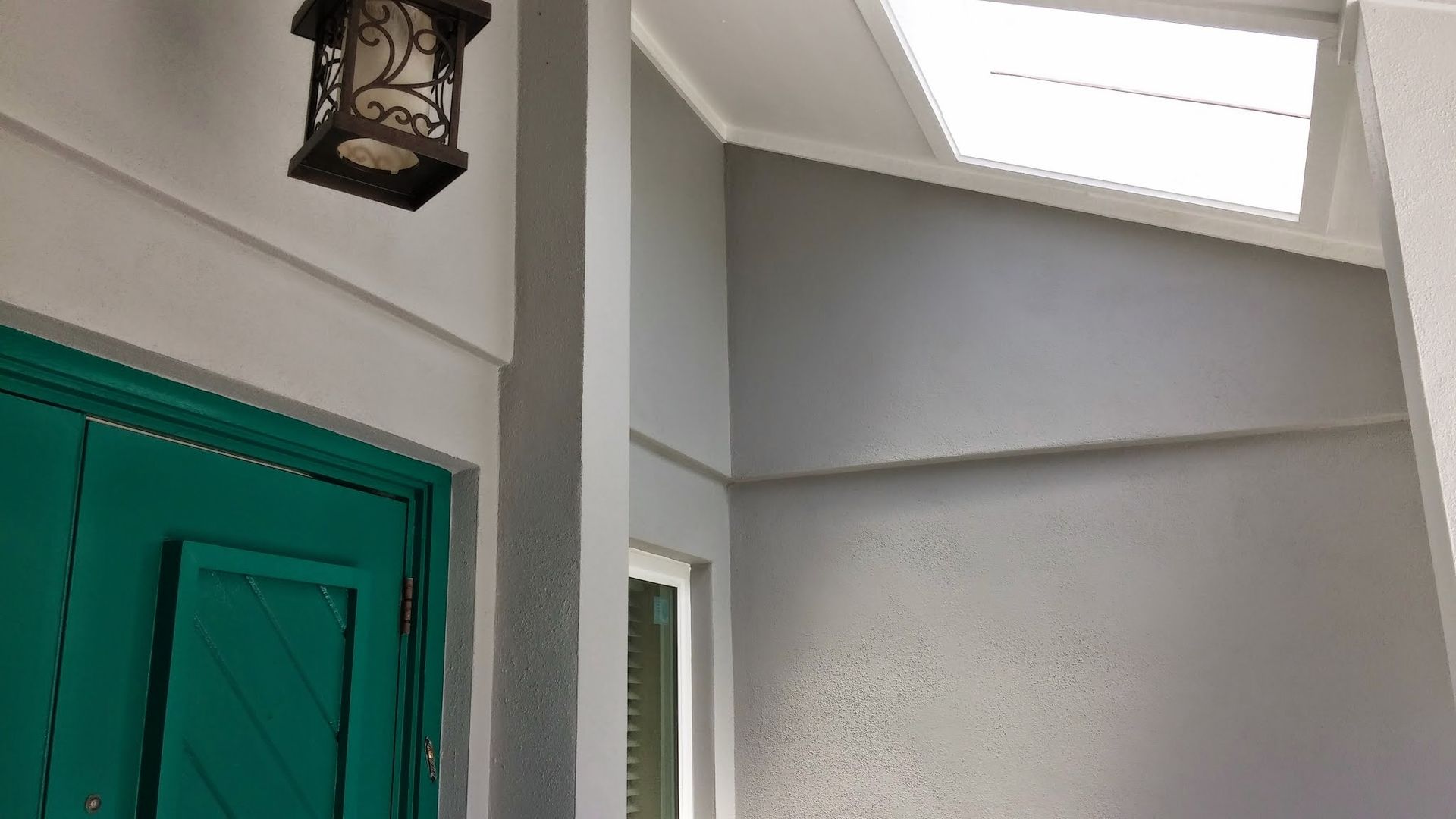 Indoor entryway with a green door, wall lantern, and skylight above a gray staircase landing