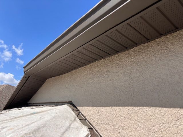 House roof eaves and stucco wall against a blue sky, with a tarp-covered object below