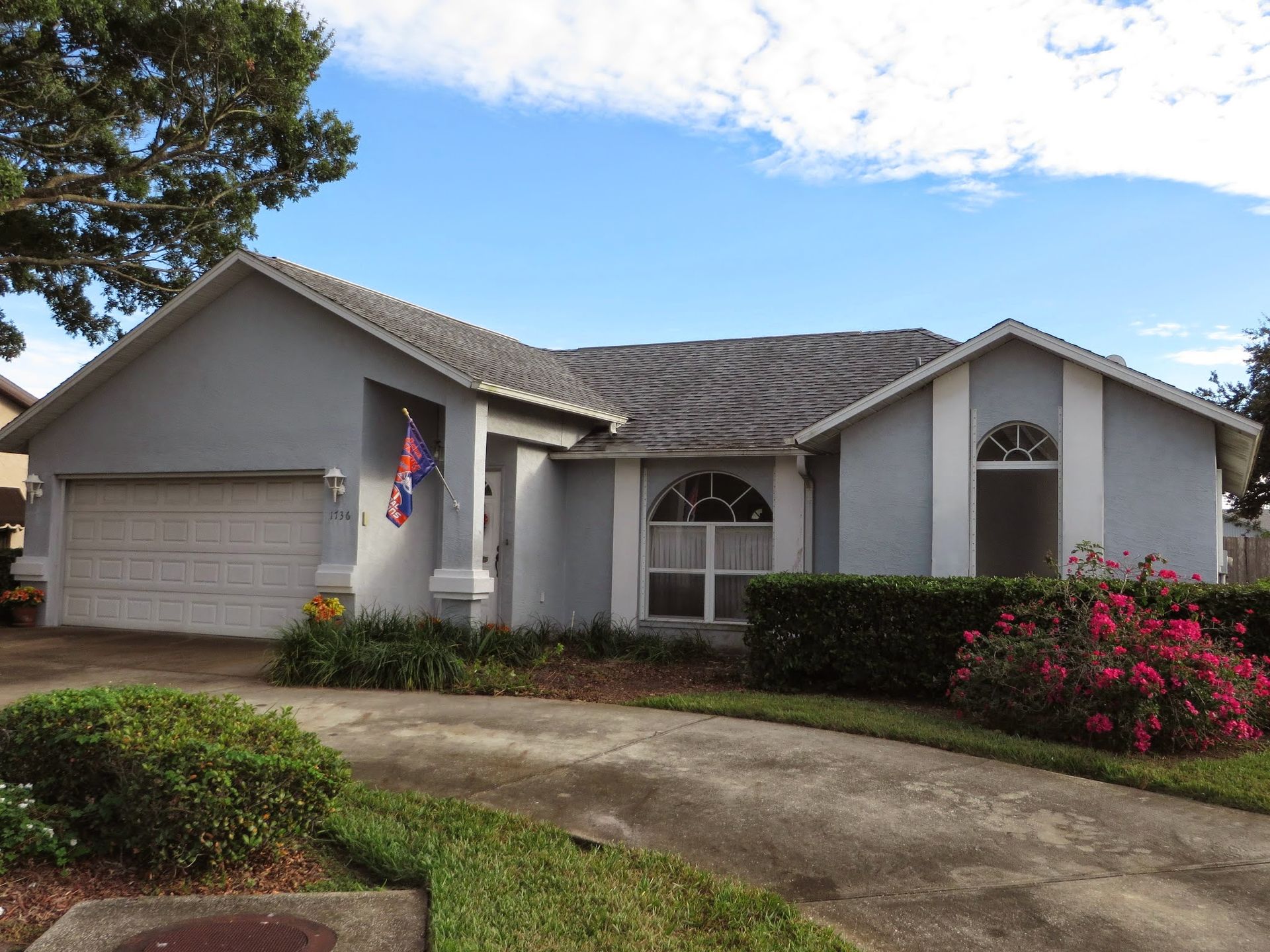 Suburban single-story house with a two-car garage, curved driveway, and flowering shrubs in front.