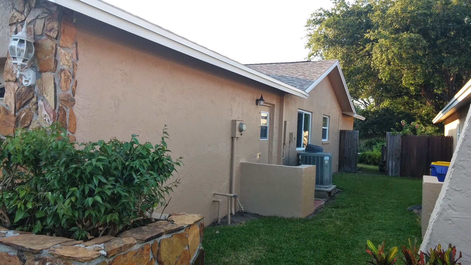 Narrow side yard beside a beige house with a hedge, outdoor AC unit, and a grassy strip leading to the back.