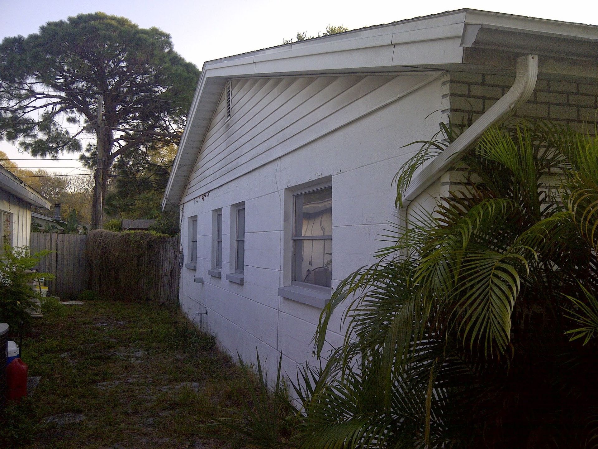 White house side exterior with small windows, surrounded by grass and trees.