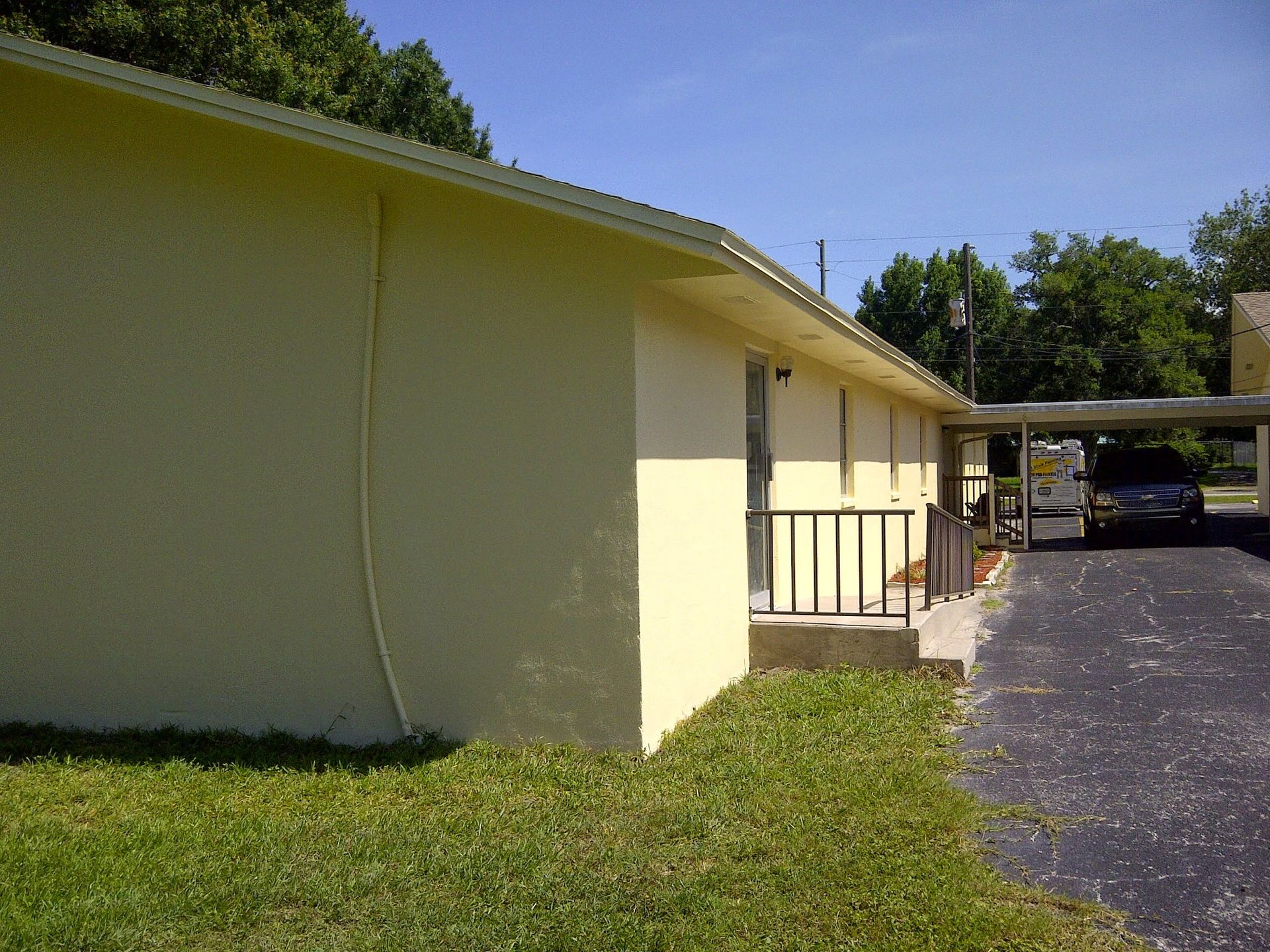 Yellow house exterior with a covered porch, driveway, and parked car beside a grassy yard