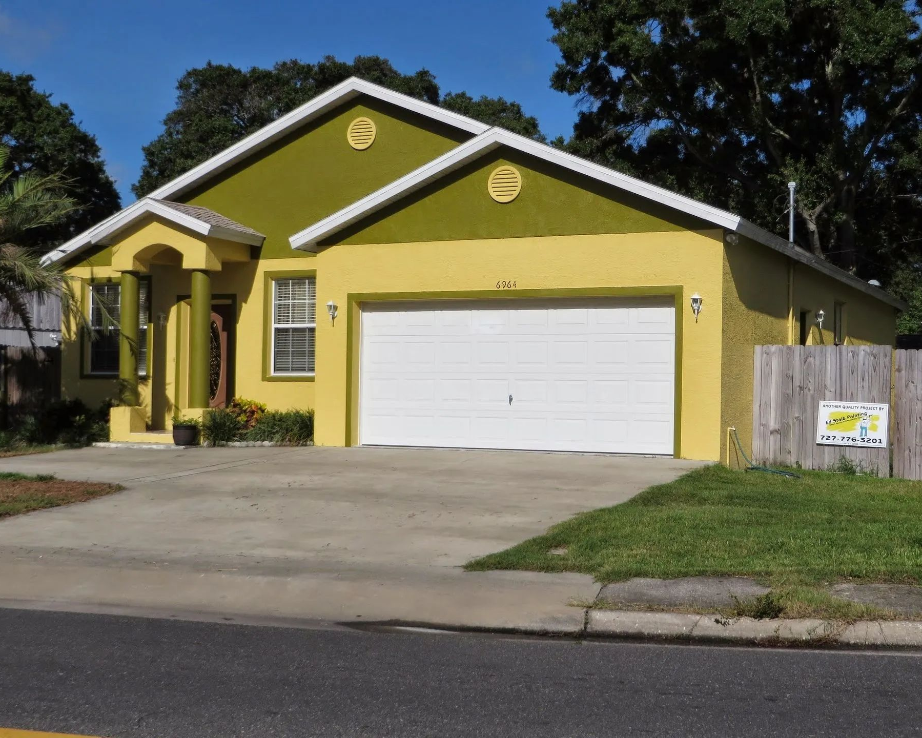 Yellow single-story house with white garage door, front porch, and driveway on a sunny street.