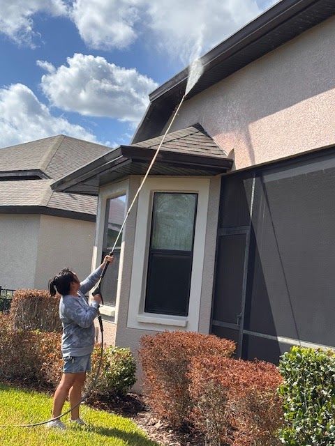 Person using a long pole to clean a second-story window outside a house