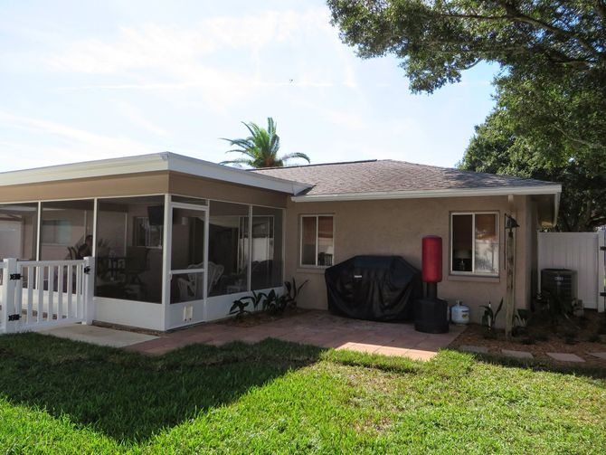 Single-story house with screened porch, covered grill, and small front yard under a sunny sky