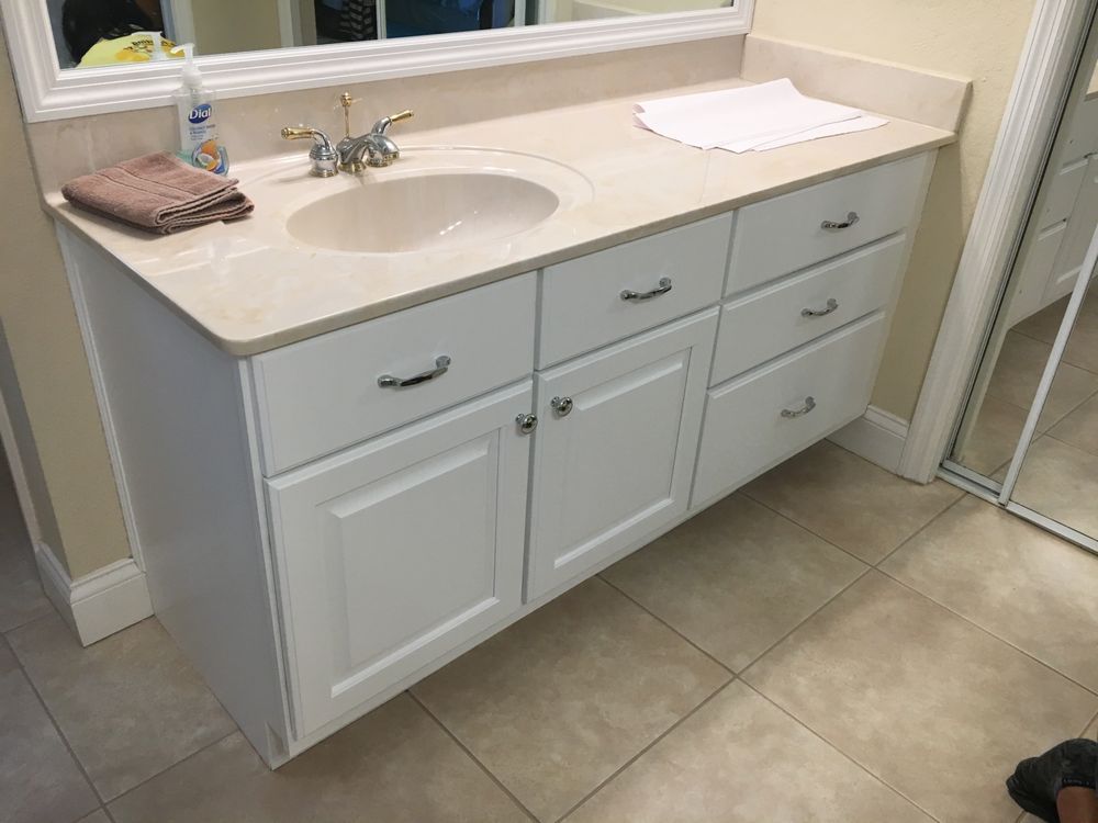 White bathroom vanity with beige countertop, sink, chrome faucet, and tiled floor.