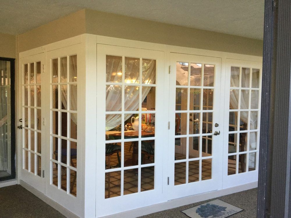 White enclosed porch with many windows and glass doors, reflecting warm indoor lights.