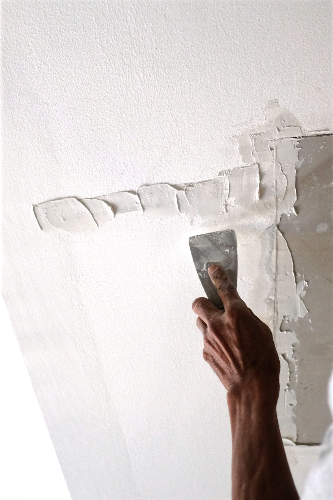 Hand scraping peeling white paint from a wall with a putty knife