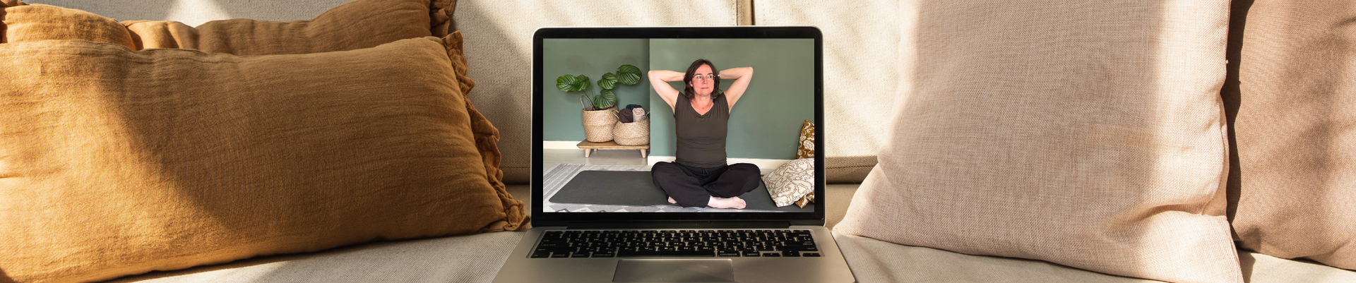 Laptop met op het scherm Astrid die op een yogamat zit, omringd door kussens.